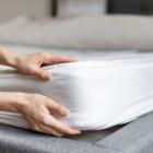 Woman putting new orthopedic mattress on sleeping bed